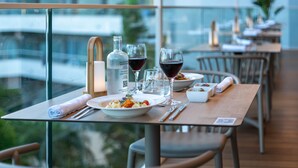 Une table à manger dressée avec des assiettes, des verres et une bouteille, donnant sur un paysage urbain.