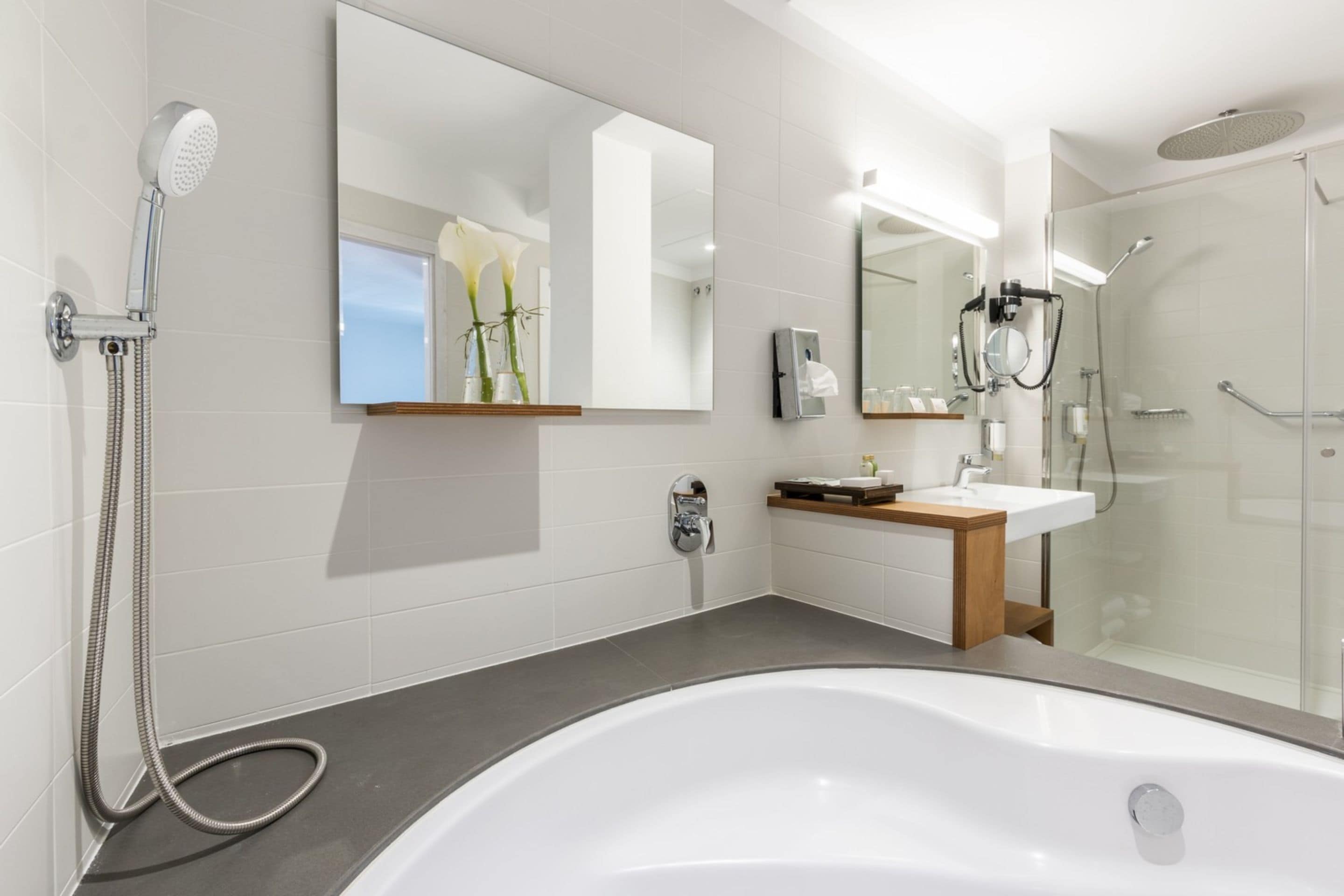 Une salle de bain moderne dotée d’une grande baignoire, d’un espace douche et d’un meuble-lavabo avec un miroir.