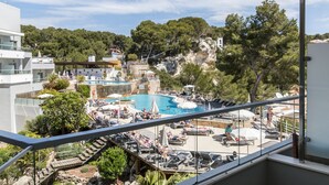 Un espace piscine doté de chaises longues et de parasols, entouré d’arbres et d’immeubles.