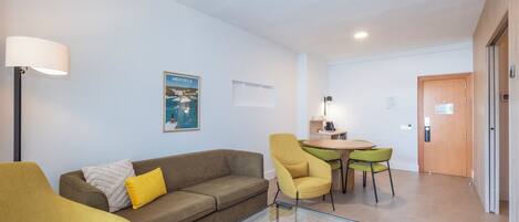 A modern living room with a sofa, armchairs, a glass coffee table, and a dining area with a table and chairs.