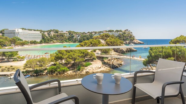 Un balcon avec deux chaises et une table, donnant sur une zone côtière avec un pont, une plage et des bâtiments.