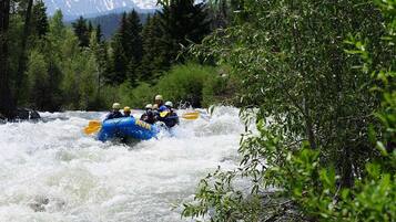 Un grupo de personas haciendo rafting en un río rodeado de árboles y montañas.