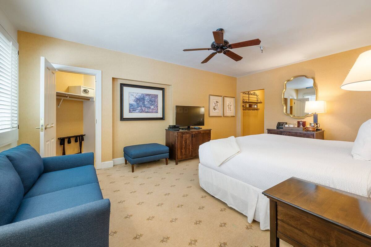 A hotel room with a bed, a blue sofa, a television, a ceiling fan, and a dresser.