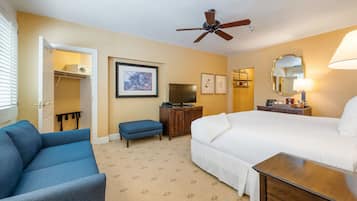 A hotel room with a bed, a blue sofa, a television, a ceiling fan, and a dresser.