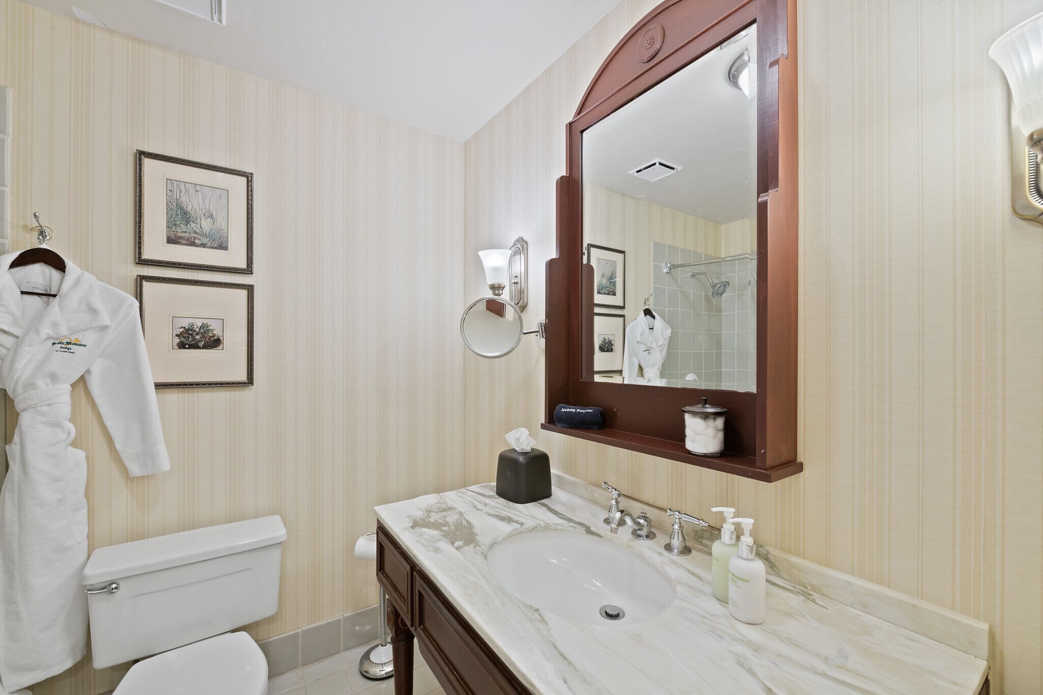 Un baño con un espejo grande, un lavabo de mármol, un inodoro y cuadros en la pared.