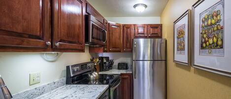 A kitchen with wooden cabinets, stainless steel appliances, a granite countertop, and framed artwork on the wall.