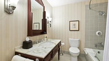 Une salle de bain avec un lavabo en marbre, un grand miroir, des toilettes et une douche dotée d’une porte en verre.