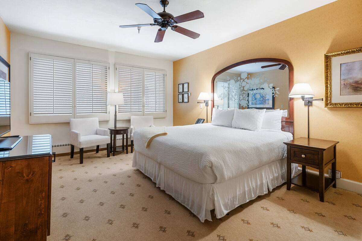 A hotel room with a large bed, a desk, a chair, a desk lamp, and a ceiling fan.