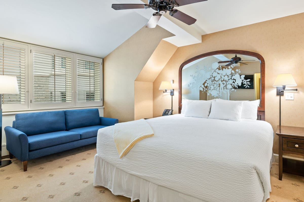 A hotel room with a large bed, a blue sofa, a ceiling fan, and a large mirror.