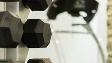 A set of black hexagonal dumbbells on a rack, with a treadmill in the background.