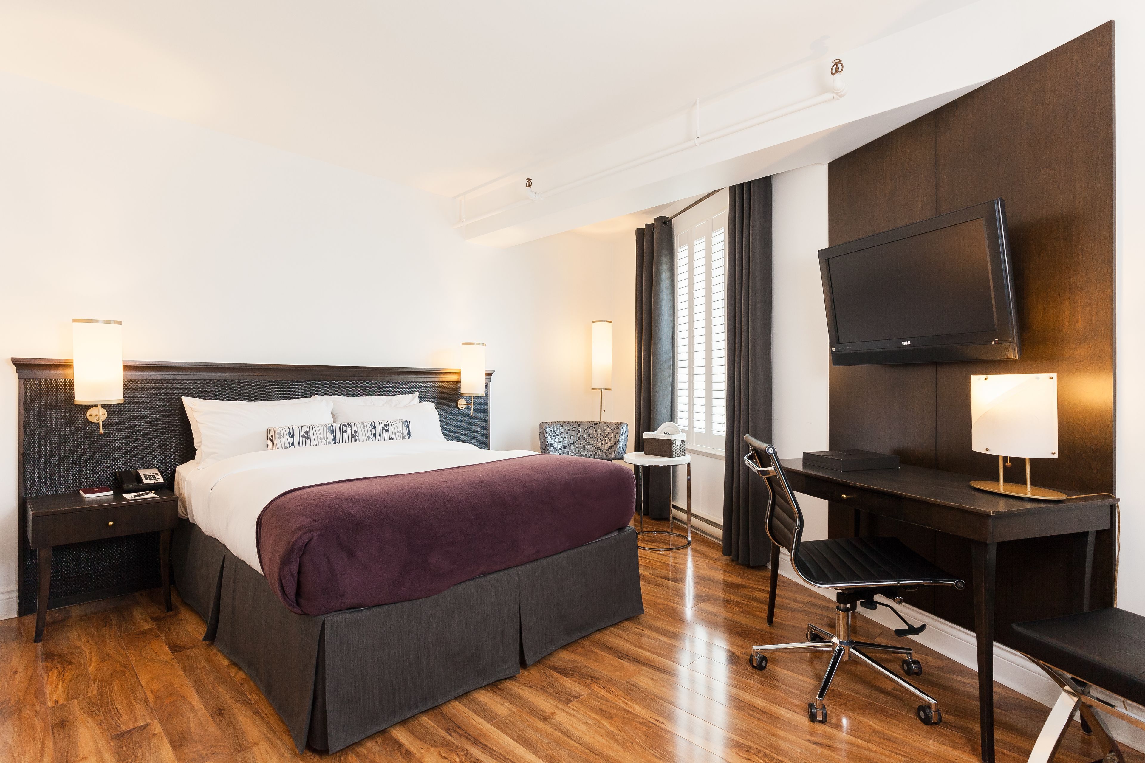 A hotel room with a large bed, a desk, a chair, a TV, and two bedside tables with lamps.