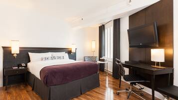 A hotel room with a large bed, a desk, a chair, a TV, and two bedside tables with lamps.