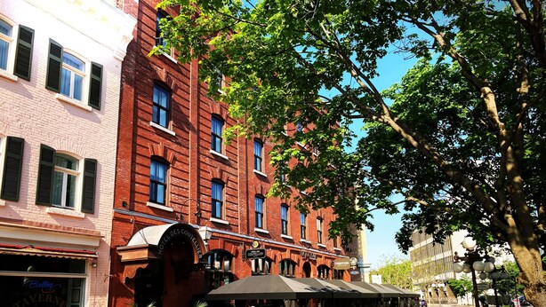 A red brick building with a restaurant patio featuring outdoor seating and potted plants.