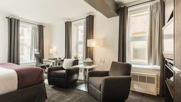 A hotel room with a bed, two armchairs, a small table, a lamp, and a window with curtains.