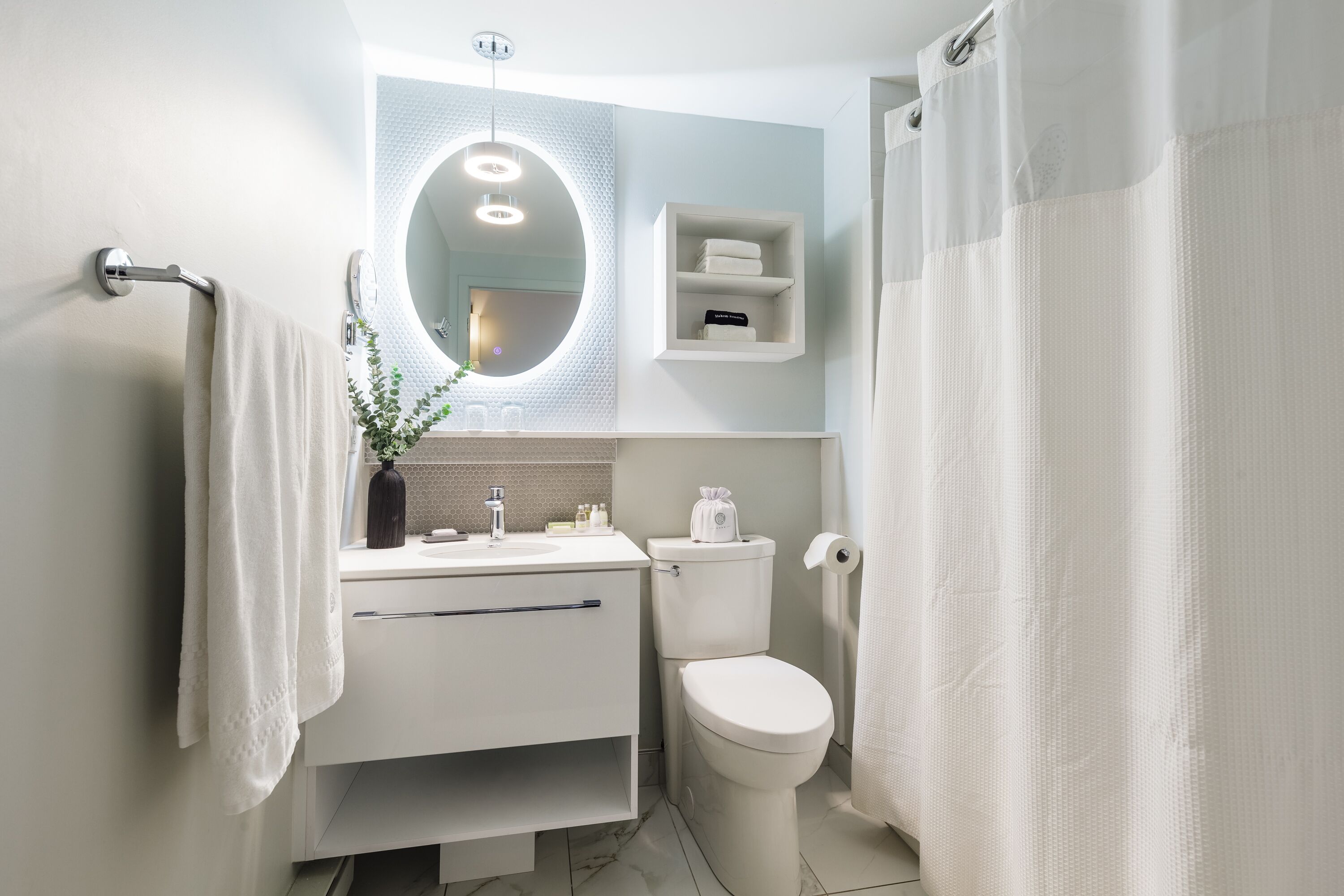 A modern bathroom with a white sink, mirror, and toilet. There is a towel rack on the left and a shower curtain on the right.