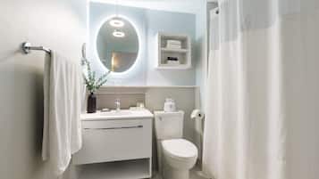 A modern bathroom with a white sink, mirror, and toilet. There is a towel rack on the left and a shower curtain on the right.