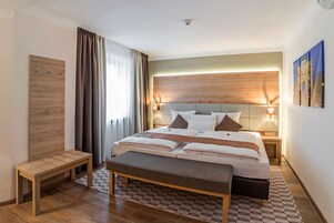 Un hotel moderno con una cama grande, lámparas de noche, un banco y vistas a la ciudad.