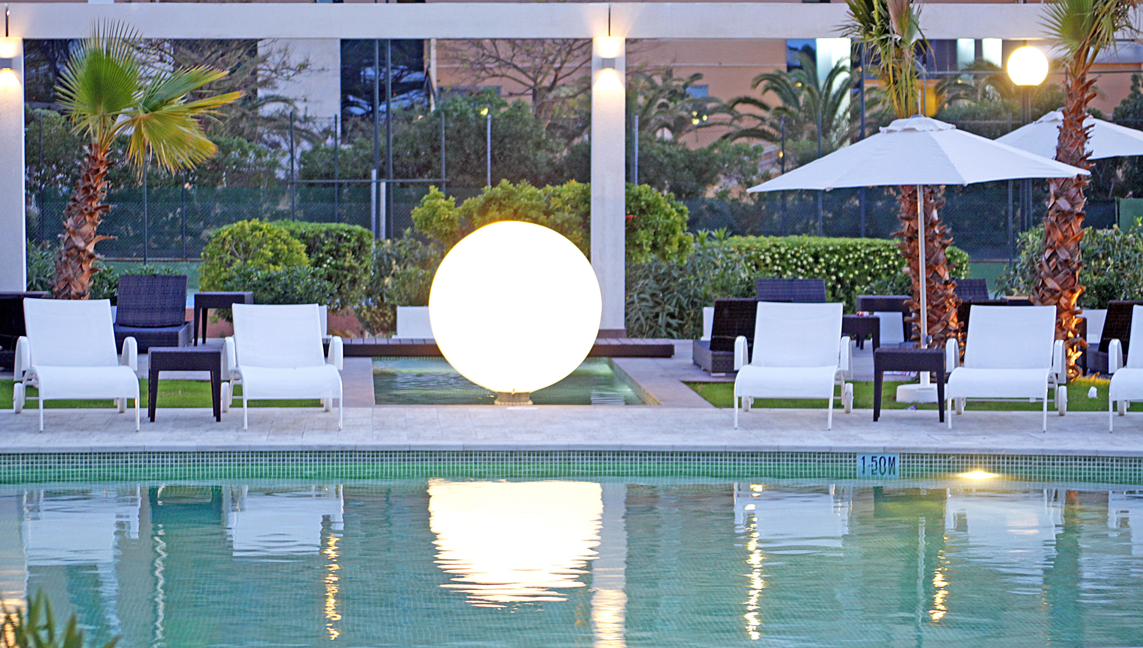 A poolside area with lounge chairs, a large illuminated sphere, and a water feature.
