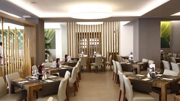 A modern restaurant with multiple dining tables and chairs, a central light fixture, and large windows with a view of the outdoors.