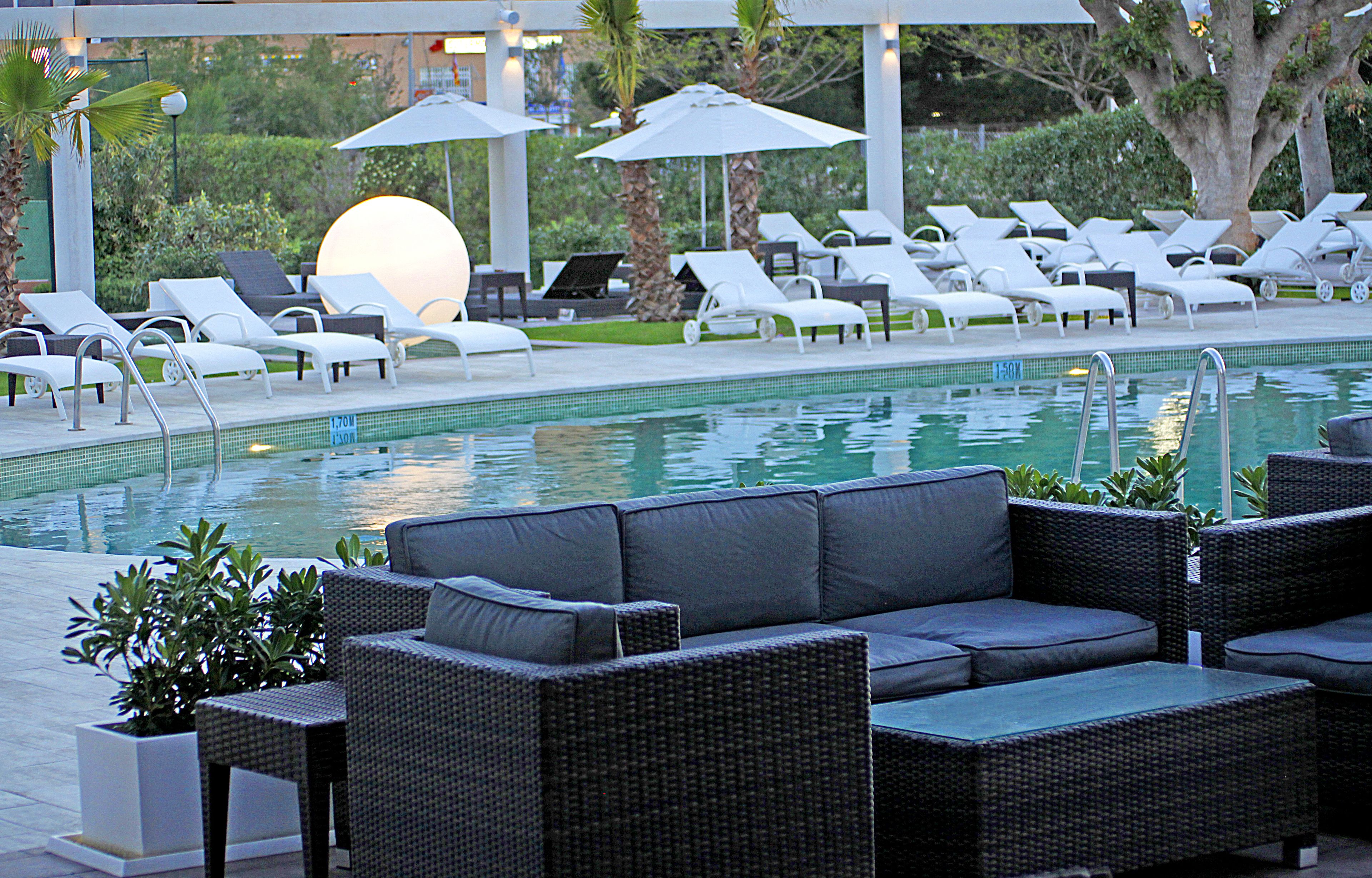 A poolside area with lounge chairs, a sofa, and umbrellas.