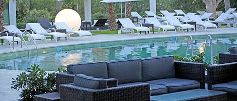 A poolside area with lounge chairs, a sofa, and umbrellas.