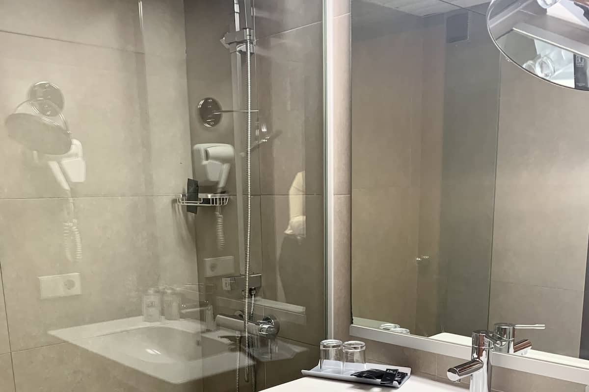 Ein modernes Badezimmer mit einer gläsernen Dusche, einem weißen Waschbecken mit Spiegel und einem Handtuch an der Wand.