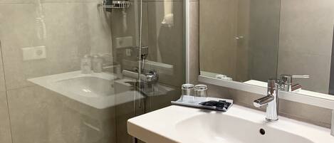 Un baño moderno con ducha de vidrio, un lavamanos blanco con espejo y una toalla colgada en la pared.
