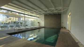 An indoor swimming pool with a wooden deck, a brick wall, and a glass wall with circular patterns.