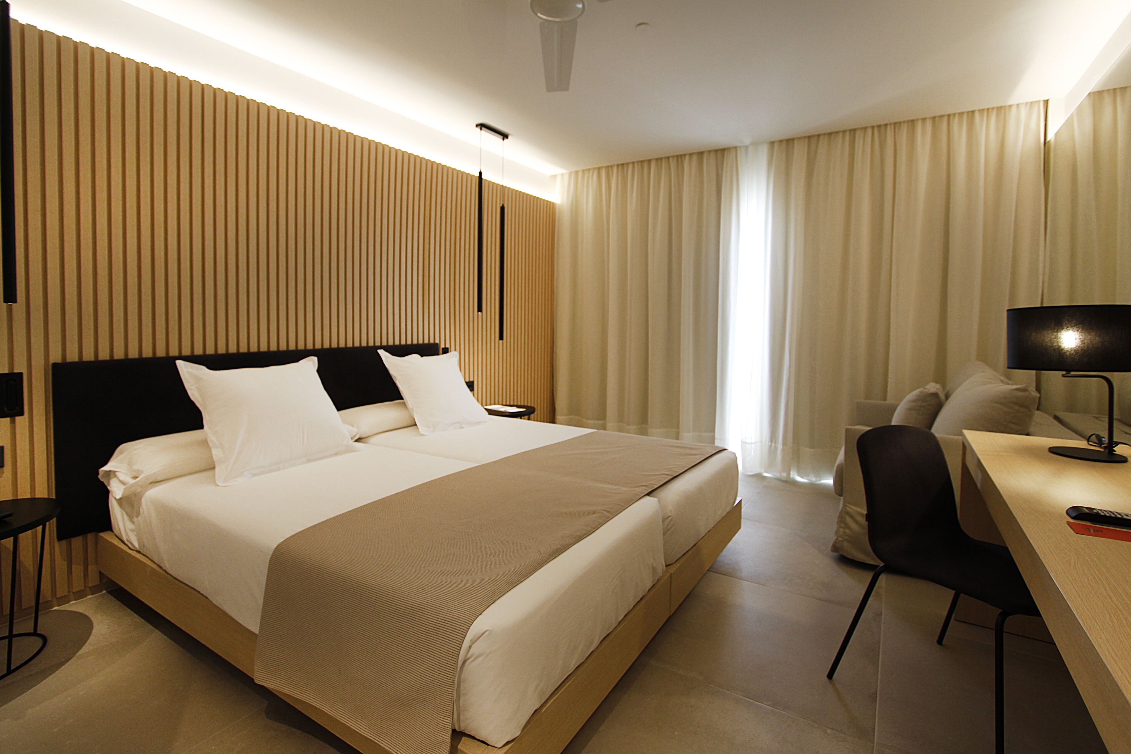 Et moderne hotelværelse med en stor seng, et skrivebord med stol og en skrivebordslampe.