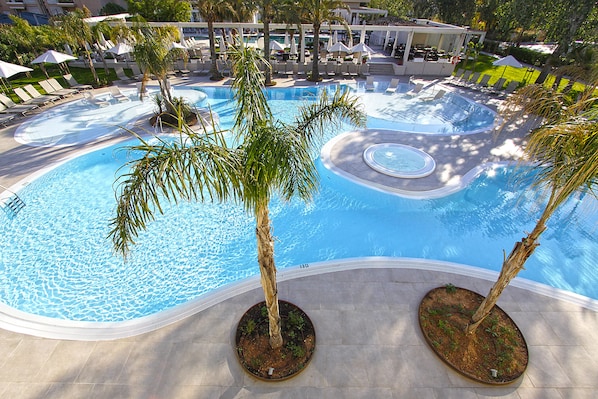Una gran piscina de varios niveles con palmeras, sillones de descanso y sombrillas.