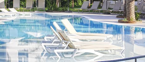 A clear swimming pool with lounge chairs and umbrellas.
