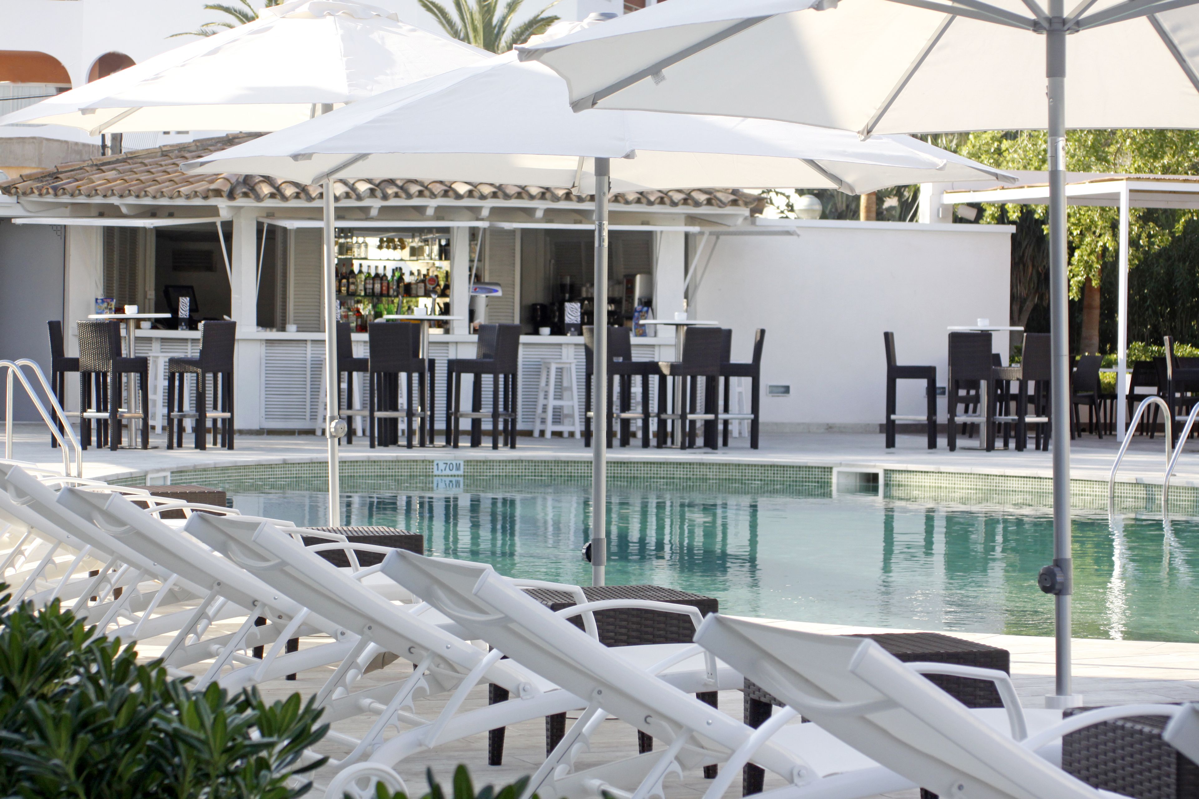 A poolside area with white lounge chairs, umbrellas, and a bar area with chairs and tables.