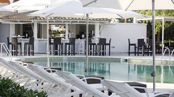 A poolside area with white lounge chairs, umbrellas, and a bar area with chairs and tables.