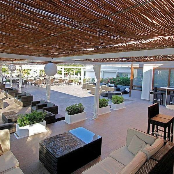 Un espacio de estar al aire libre con mobiliario moderno, techo de paja y vistas del paisaje circundante.