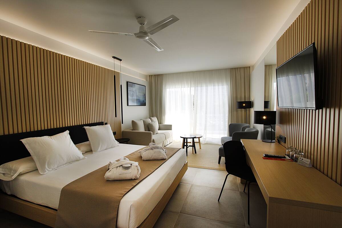 Ein Hotelzimmer mit einem Bett, einem Schreibtisch, einem Sessel, einem Fernseher und einem Deckenventilator.