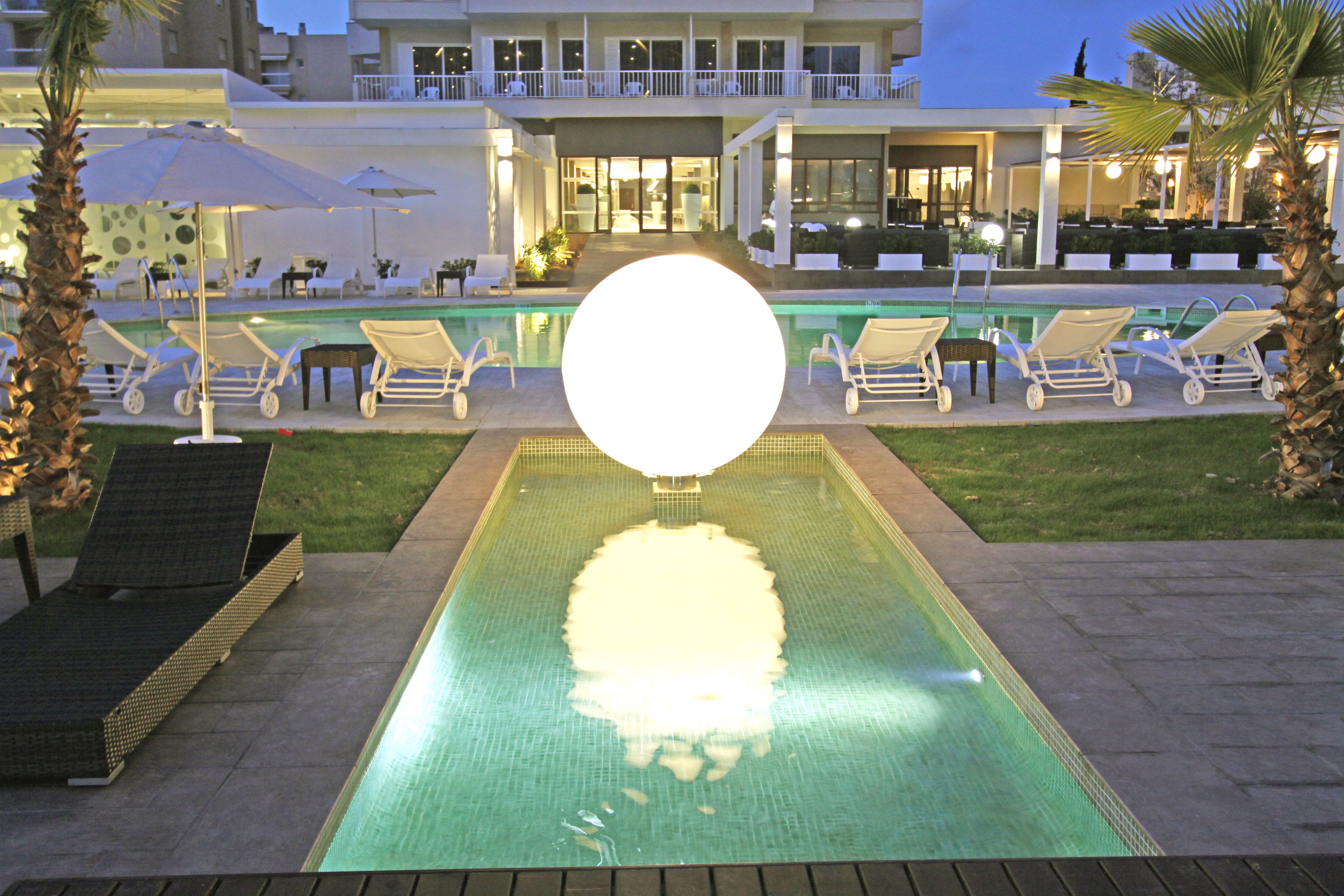 Zona de piscina amb gandules i ombrelles, envoltada per un edifici amb un balcó.