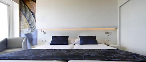 Una habitación de hotel con una cama, dos almohadas, una mesita de noche con lámpara y una silla.