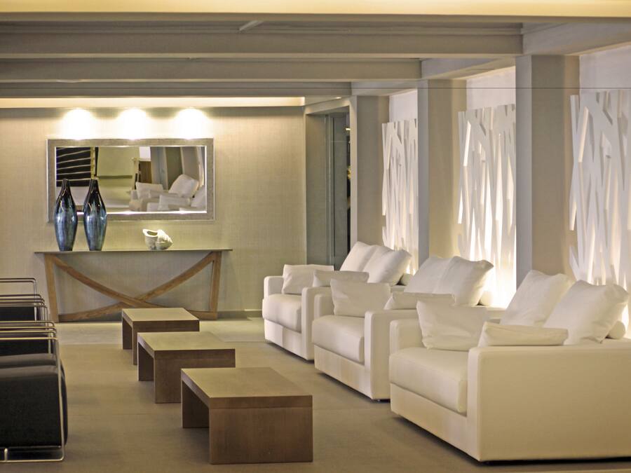A modern hotel lobby with a seating area, a reception desk, and a large mirror.
