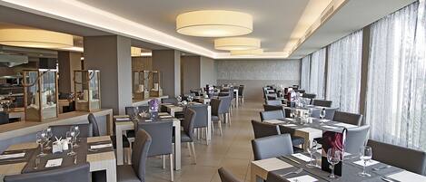 A spacious restaurant with multiple dining tables and chairs, large windows, and modern lighting fixtures.