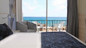 Ein Hotelzimmer mit Bett, Stuhl, Tisch und einem Balkon mit Meerblick.