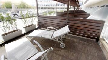 Un balcón con sillones blancos para lounge, un banco de madera y plantas en macetas.