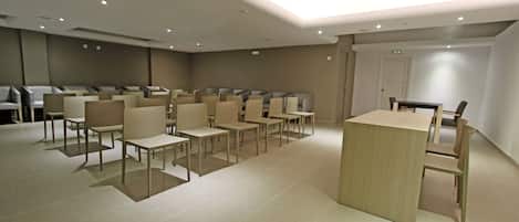 Un salón de conferencias con filas de sillas y mesas, un atril de madera y una lámpara en el techo.