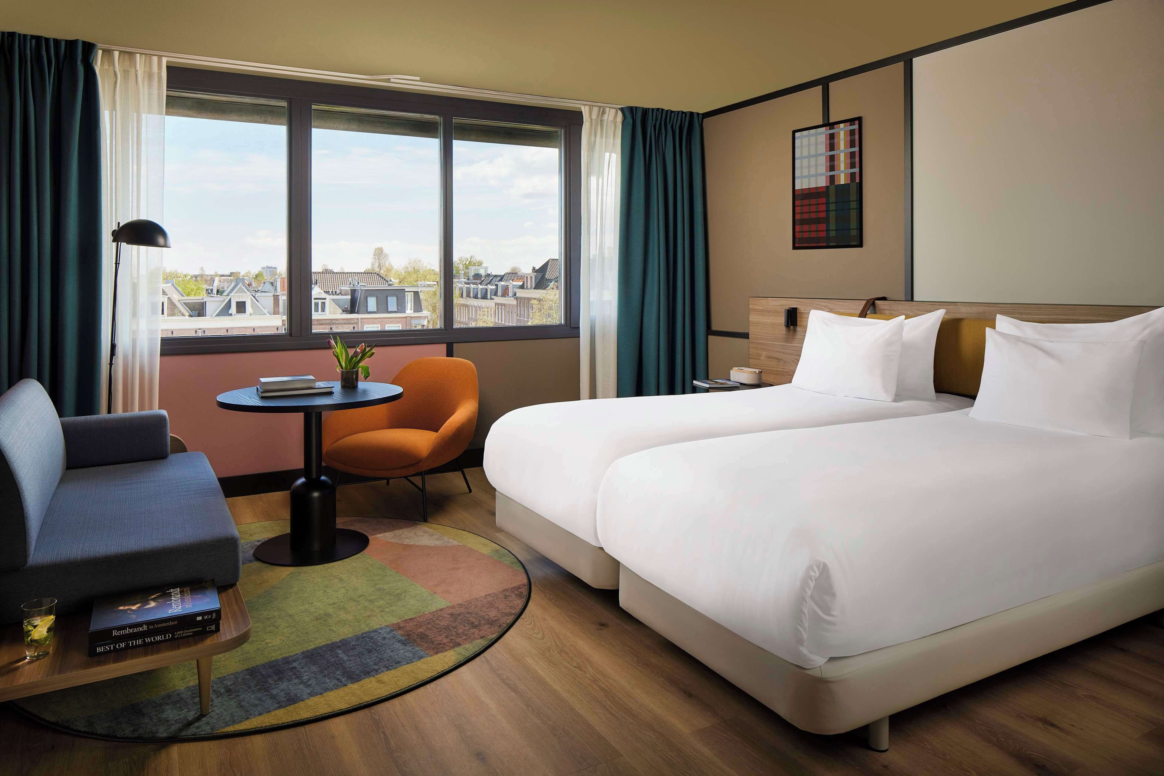 A hotel room with a large bed, a sofa, a small table, and a chair.
