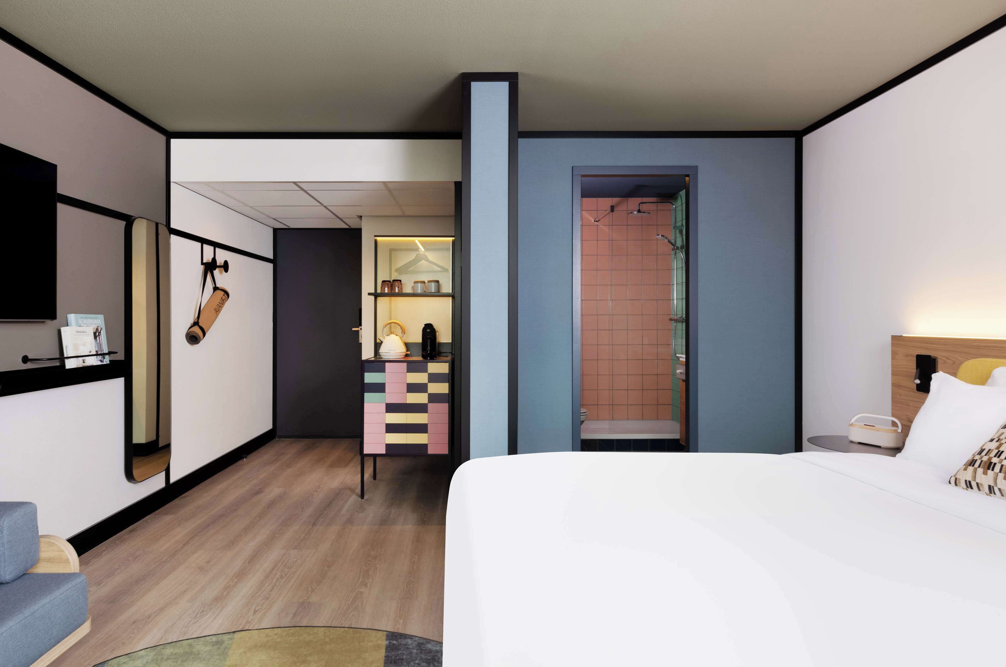 Habitación de hotel con cama, escritorio, silla, mesita y baño con ducha.