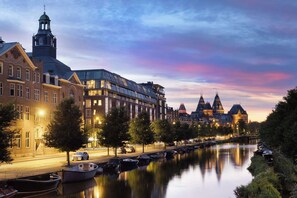 A riverside view of historic buildings with a modern glass structure, a canal with boats, and a bridge. - Avani Museum Quarter Amsterdam Hotel (Amsterdam)