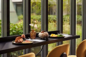 A breakfast table with croissants, bread, a plate of fruit, and a vase with flowers.