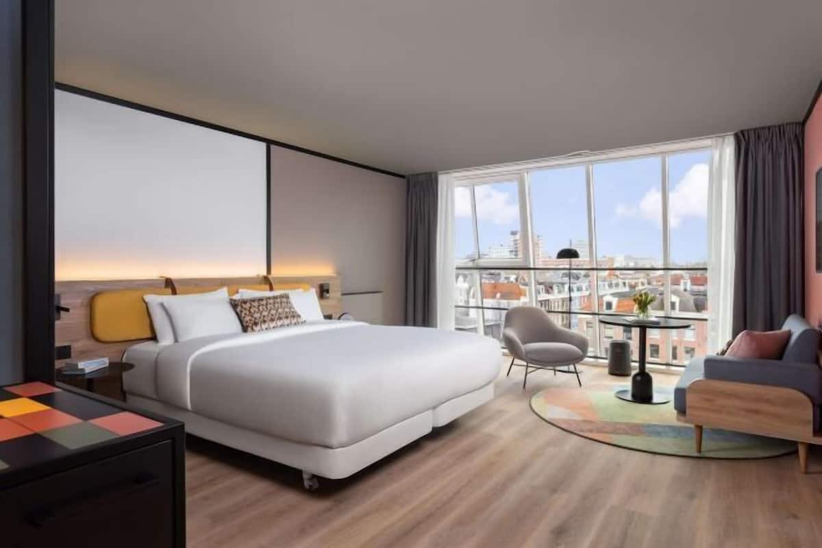 Une chambre d’hôtel moderne dotée d’un grand lit, d’un bureau, d’une chaise, d’un canapé et d’un balcon offrant une vue sur la ville.