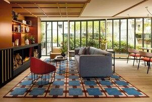 A modern living room with a fireplace, a sofa, a coffee table, and a view of a garden through large windows.