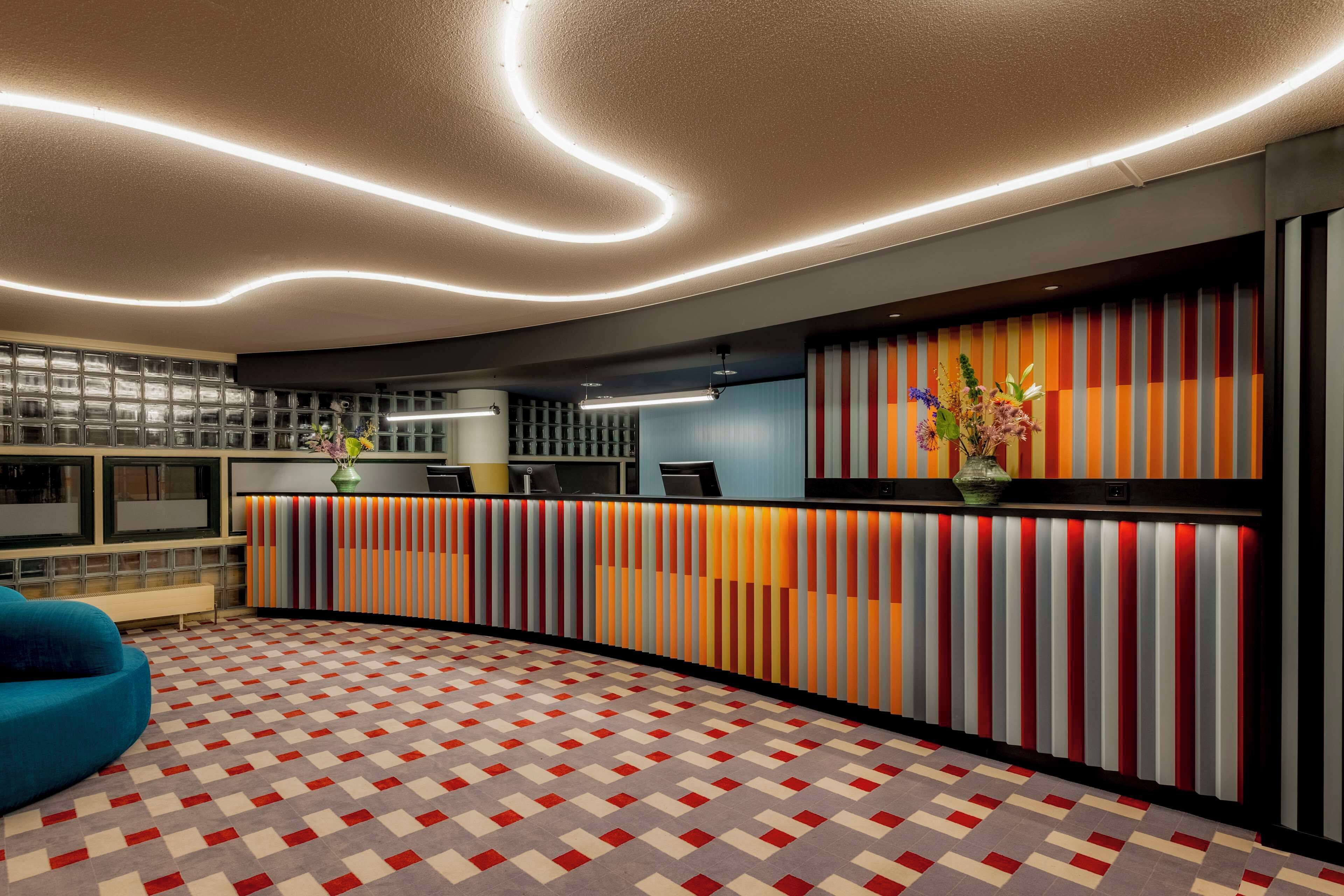Et receptionsområde med en skranke til indtjekning, et mønstret gulv og et moderne loftdesign.