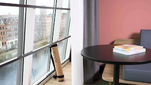 Une chambre moderne avec une grande fenêtre, une table ronde sur laquelle repose un livre et une serviette enroulée.